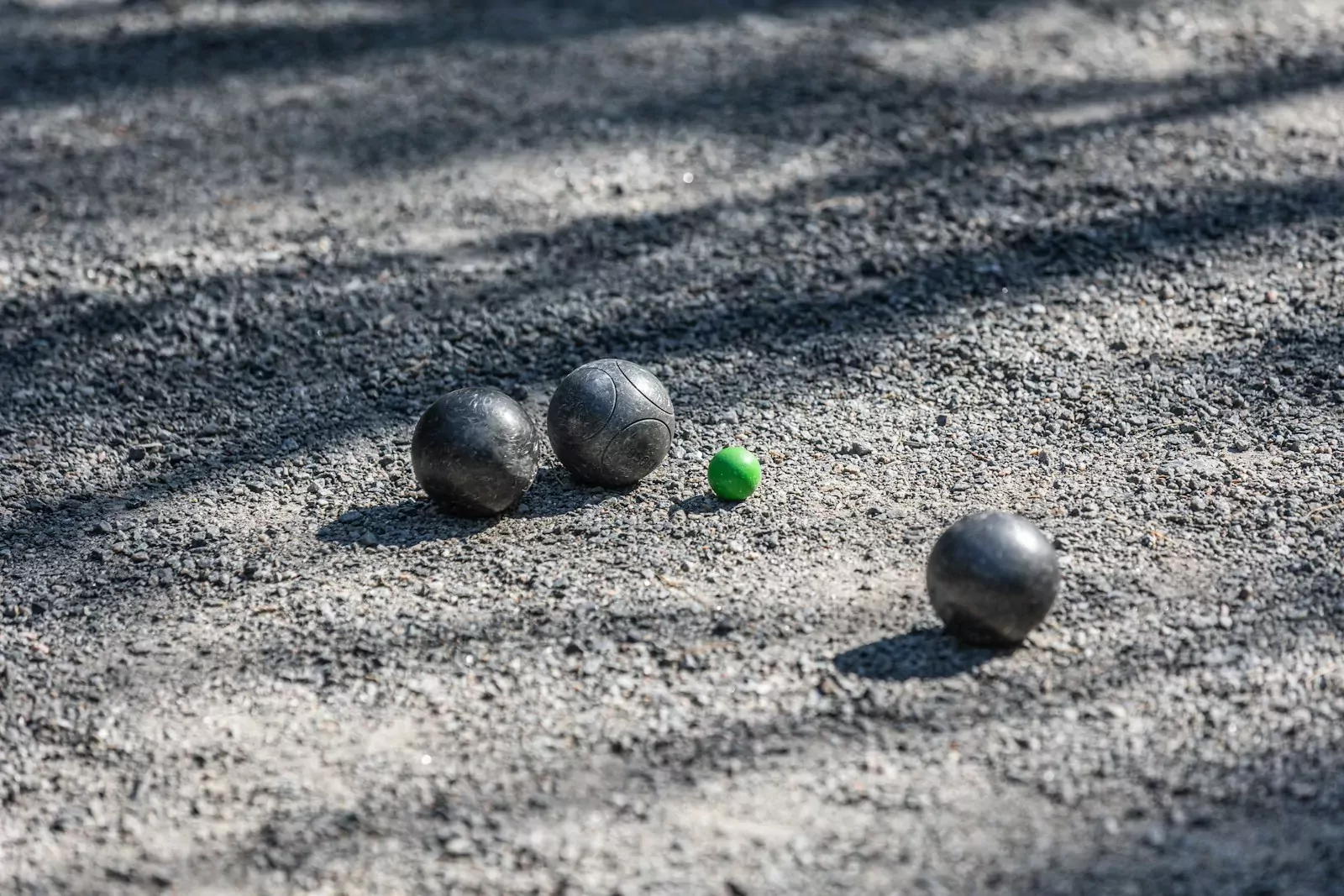 Three metal boules and a small green cochonnet on a gravel court